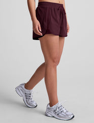 Woman wearing a white tank top and maroon shorts on a plain background