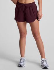 Woman wearing a white tank top and maroon shorts on a plain background