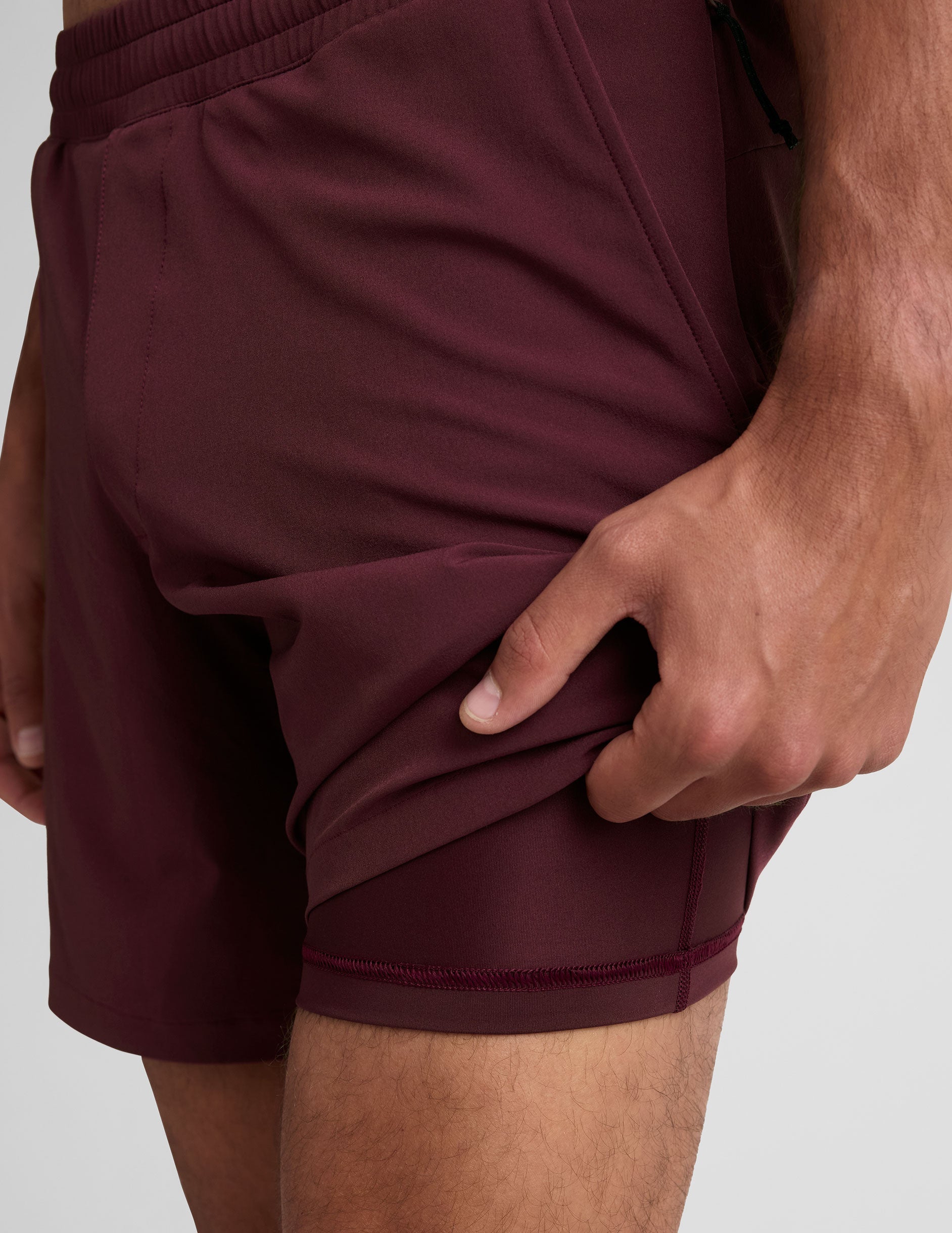 man wearing a grey t-shirt and maroon lined shorts set on a white background.