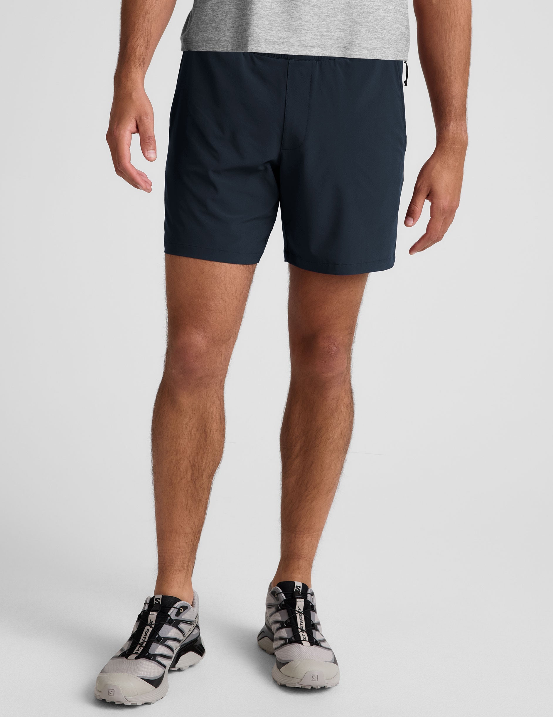 man wearing a grey t-shirt and navy blue lined shorts set on a plain background.