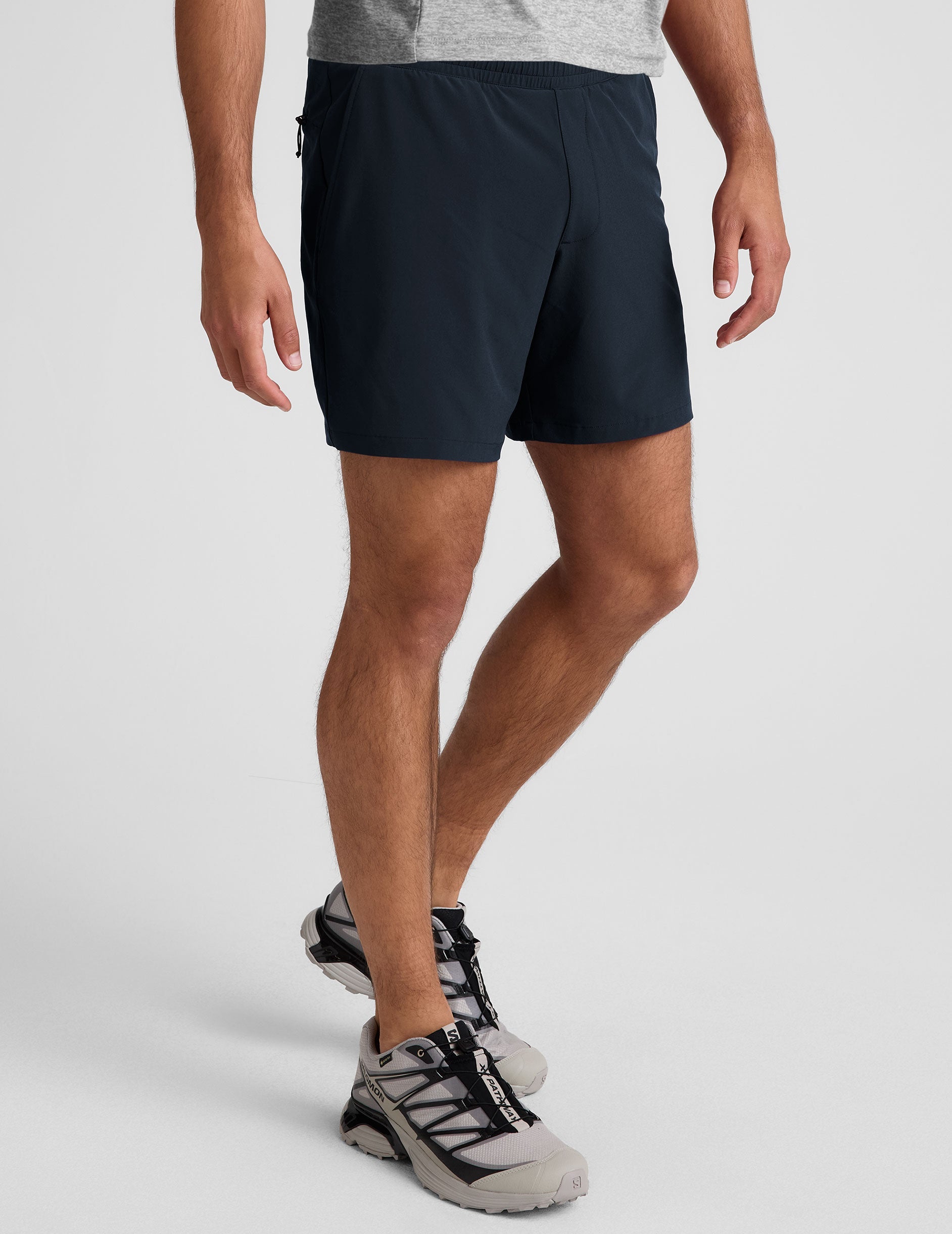 man wearing a grey t-shirt and navy blue lined shorts set on a plain background.