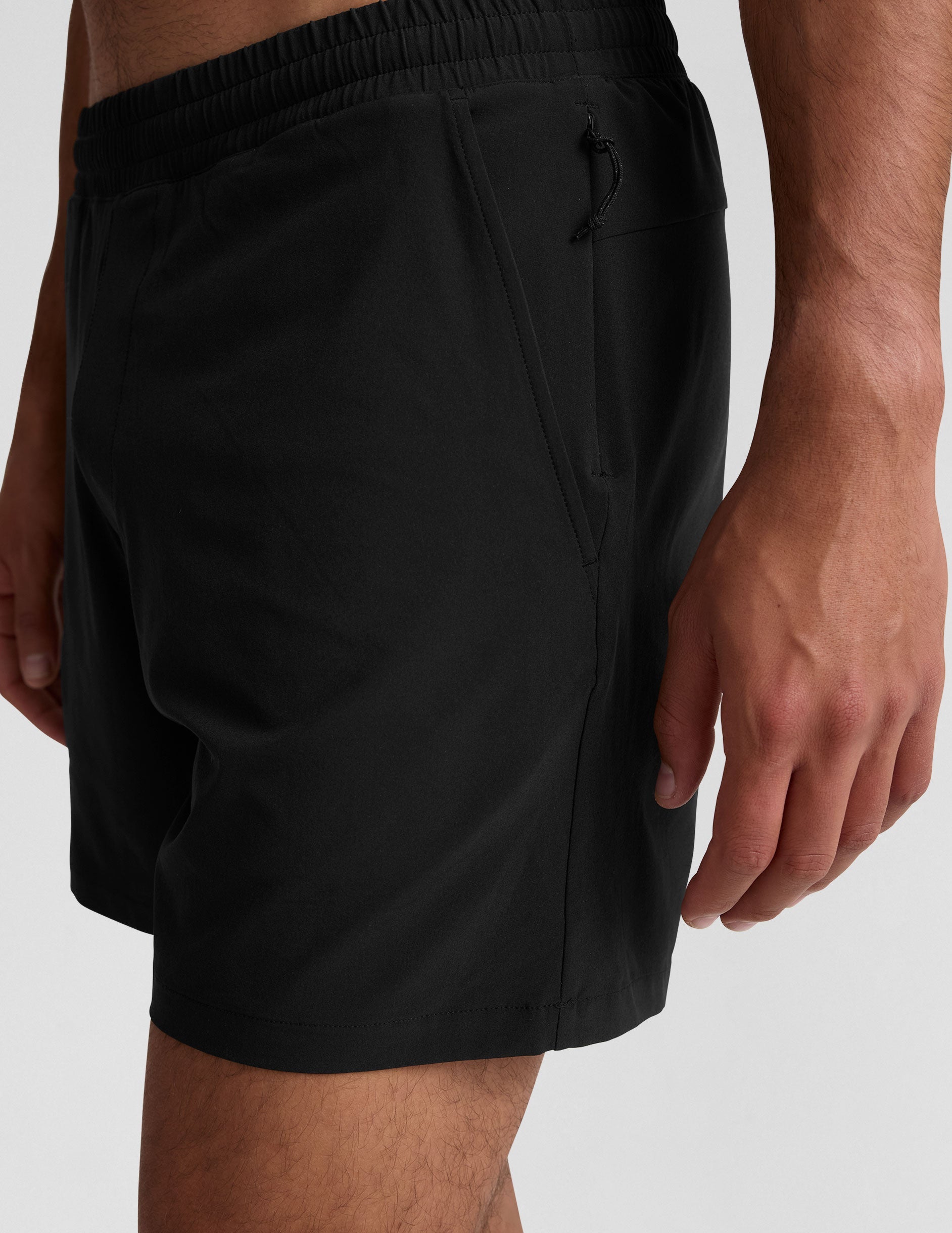 man wearing a grey crew neck t-shirt and black lined shorts on a light gray background.
