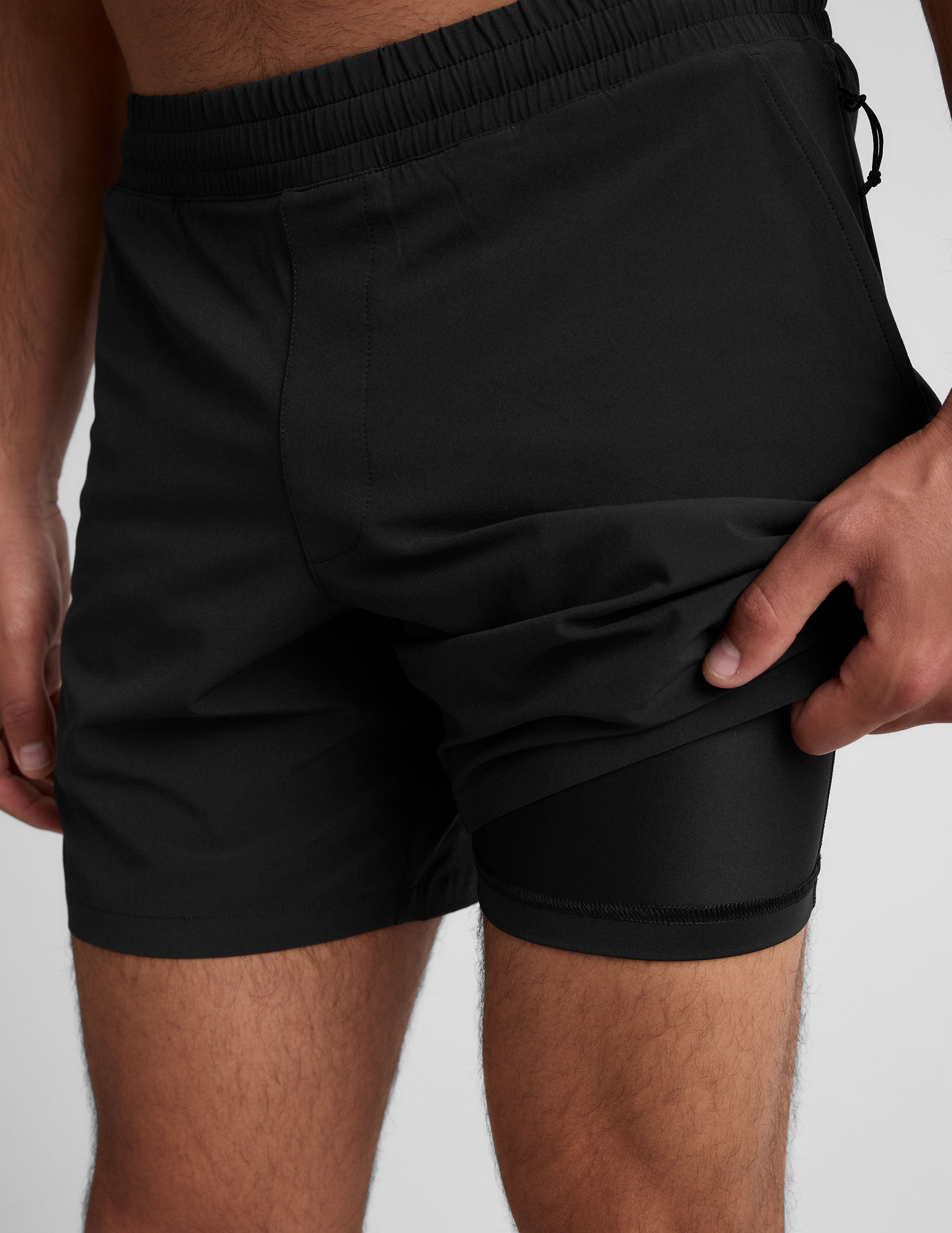man wearing a grey crew neck t-shirt and black lined shorts on a light gray background.
