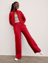 Person in a red jacket with white piping and red pants against a plain background.