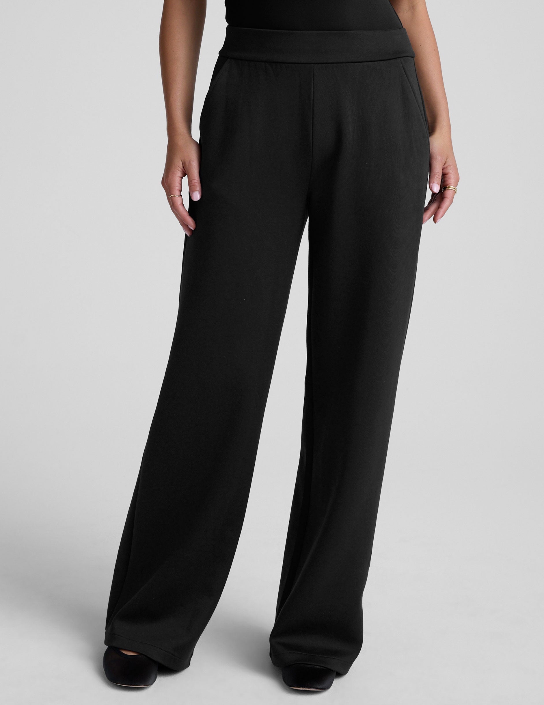 model is wearing a black sleeveless top and black spacer style pants with pockets against a plain background.