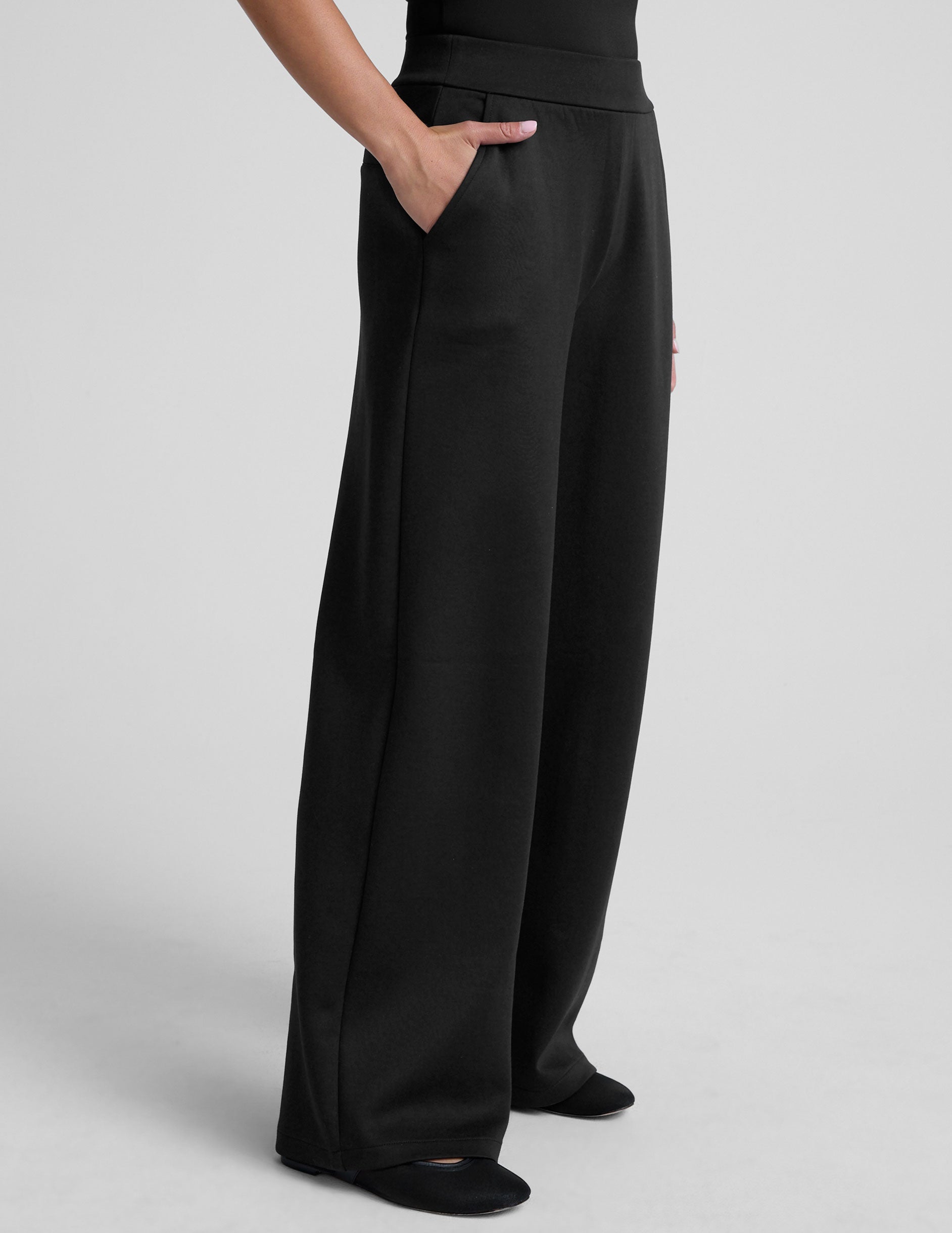 model is wearing a black sleeveless top and black spacer style pants with pockets against a plain background.
