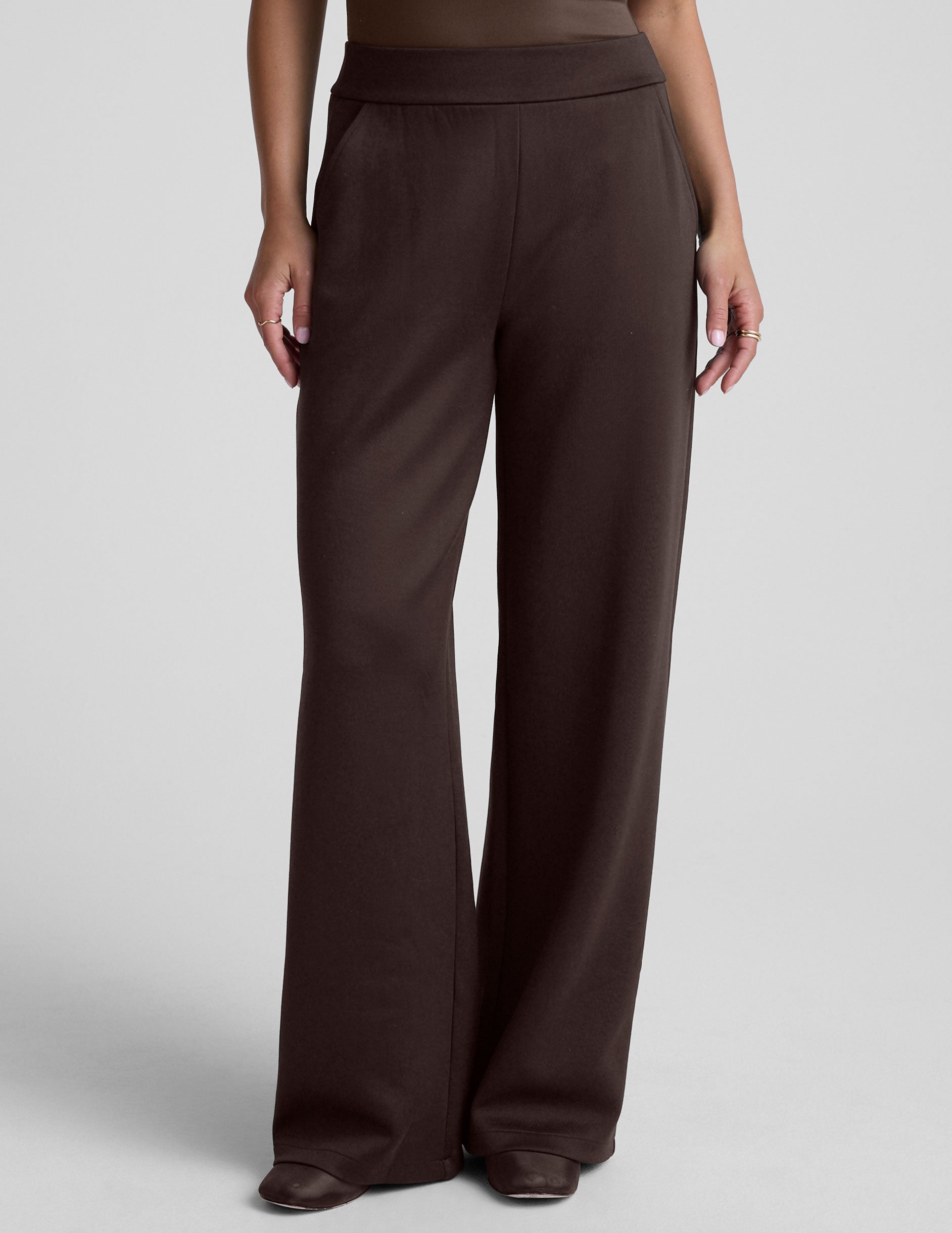 woman wearing brown wide-leg pants against a plain background.