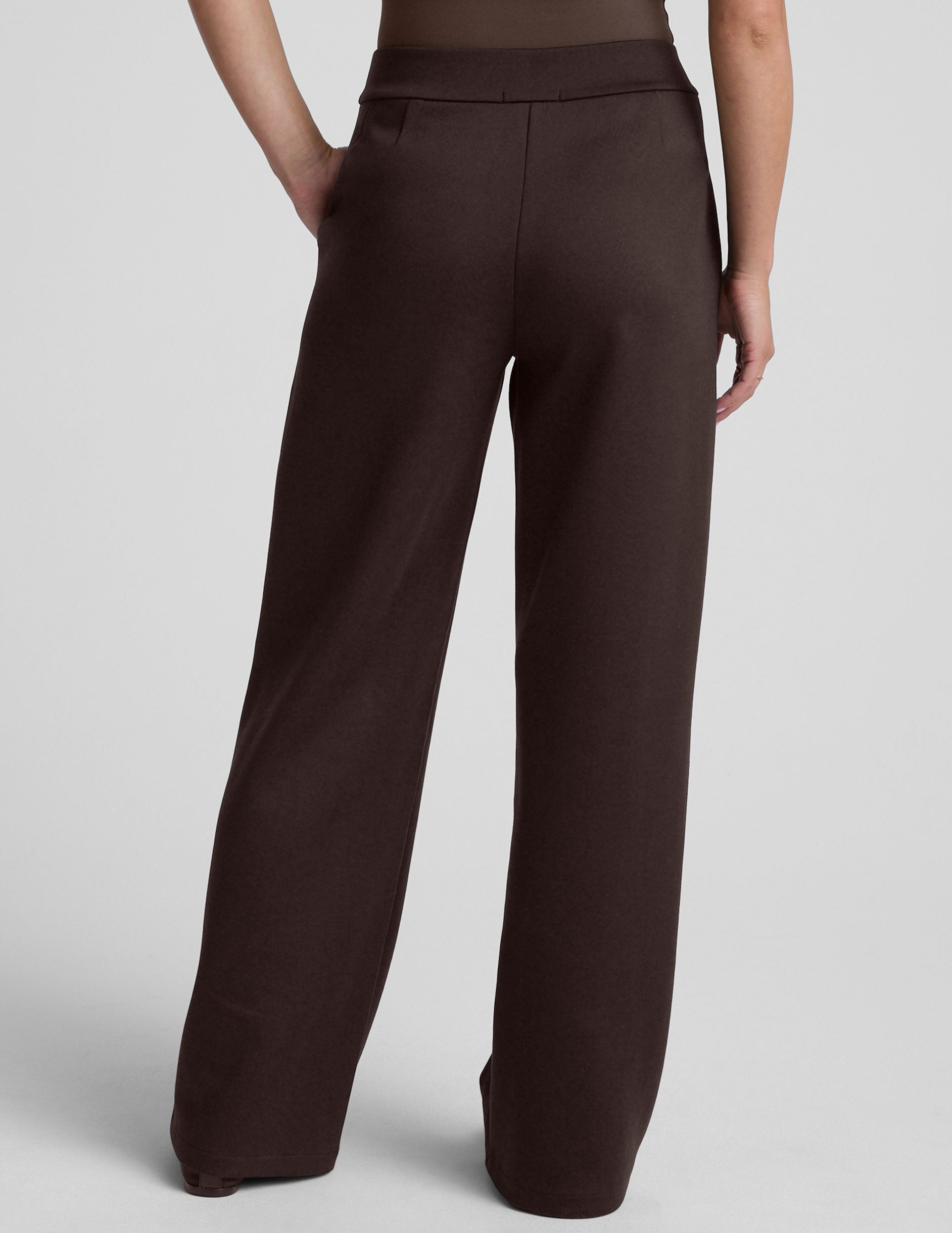 woman wearing brown wide-leg pants against a plain background.
