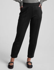 woman wearing a gray turtleneck and black tapered pants on a white background.