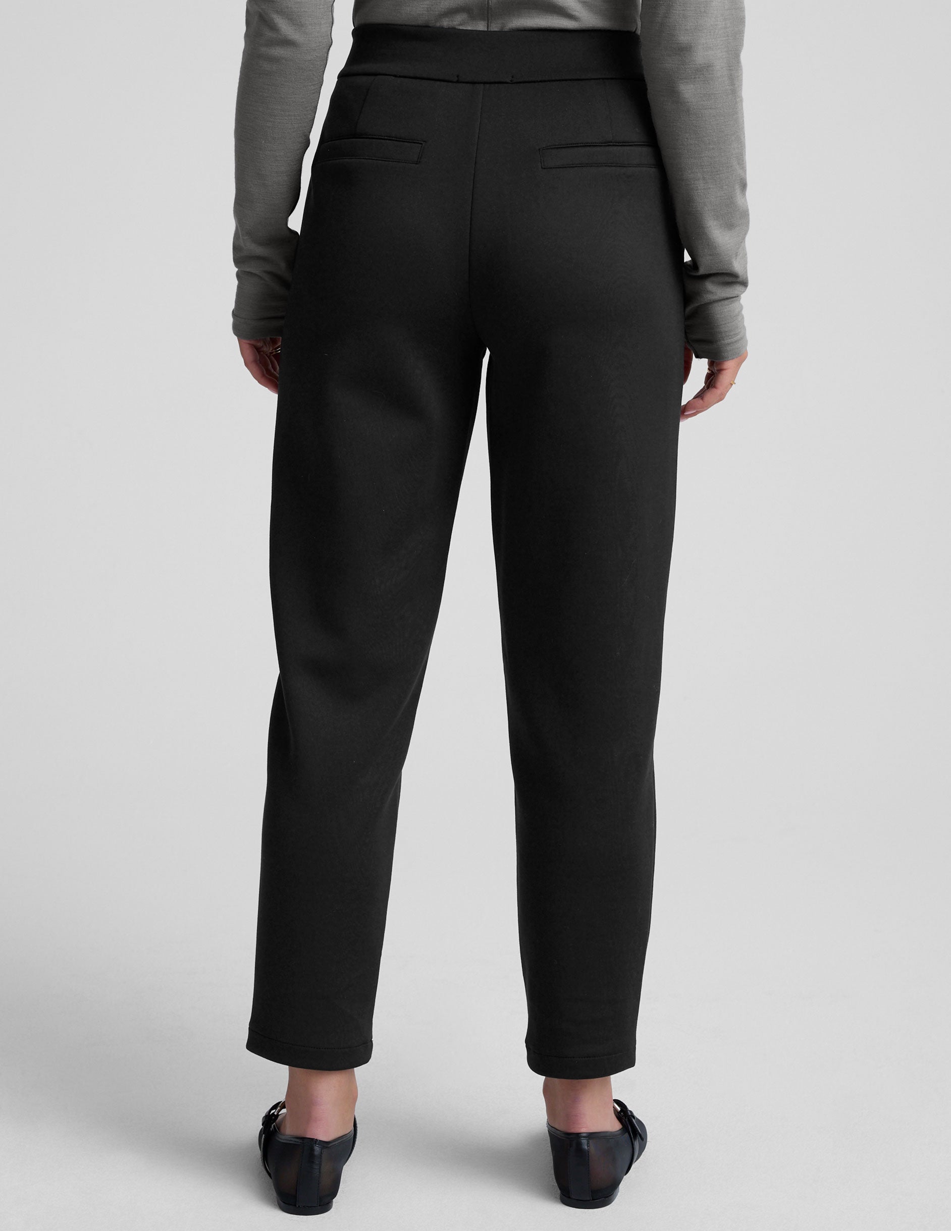 woman wearing a gray turtleneck and black tapered pants on a white background.