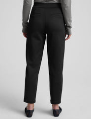 woman wearing a gray turtleneck and black tapered pants on a white background.