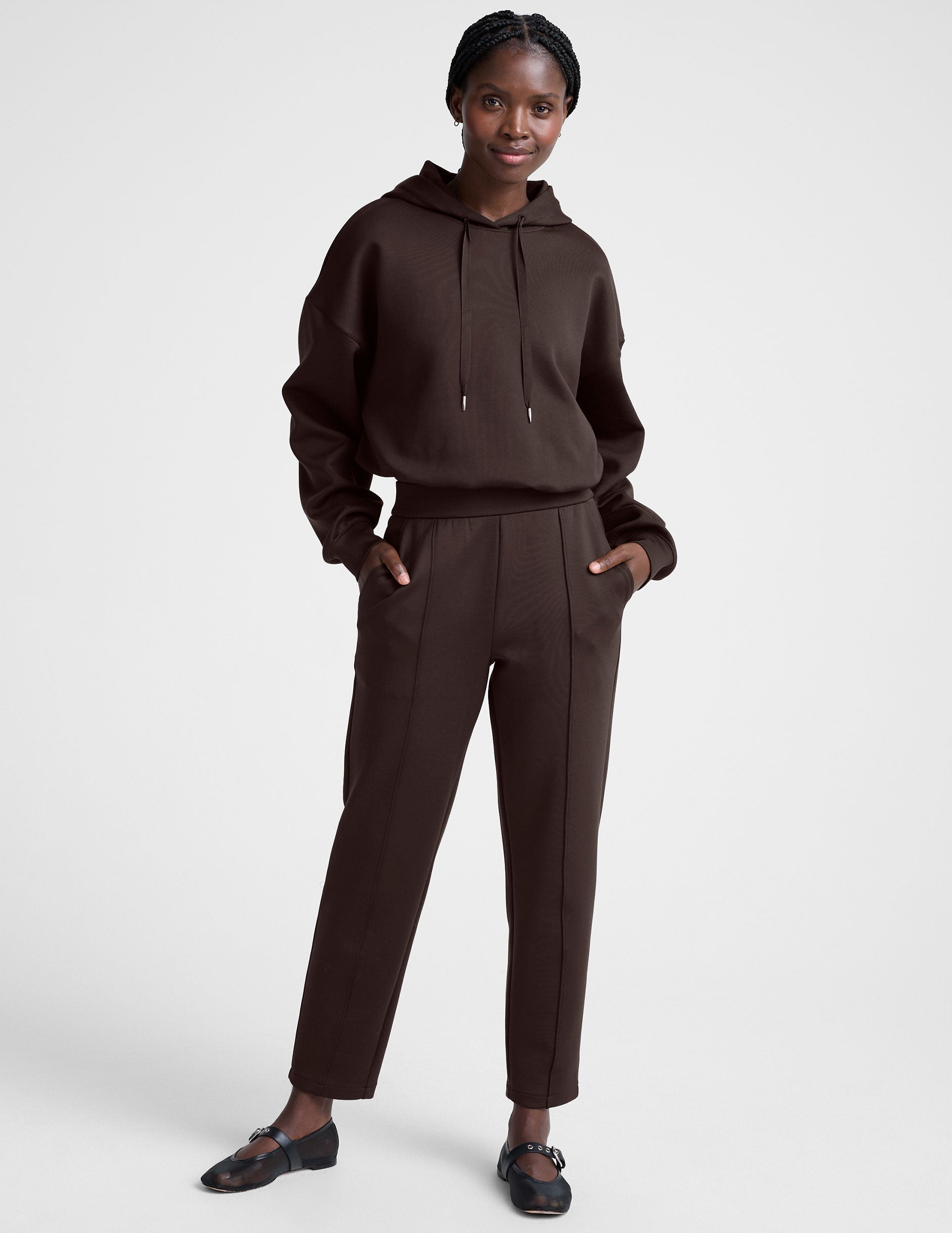 woman wearing brown tapered pants against a plain background.