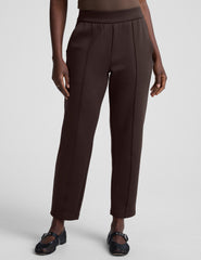 woman wearing brown tapered pants against a plain background.
