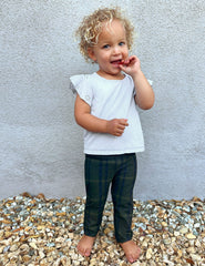 model wearing a white top and green plaid pants standing on gravel against a light gray wall.