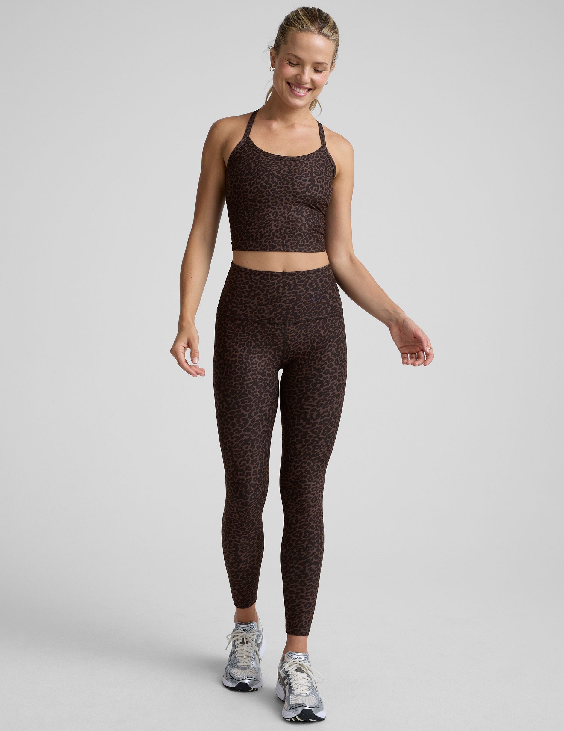 woman wearing a brown leopard print cropped tank and leggings on a gray background.