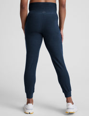 pregnant woman wearing navy blue maternity joggers with pockets on a plain background.
