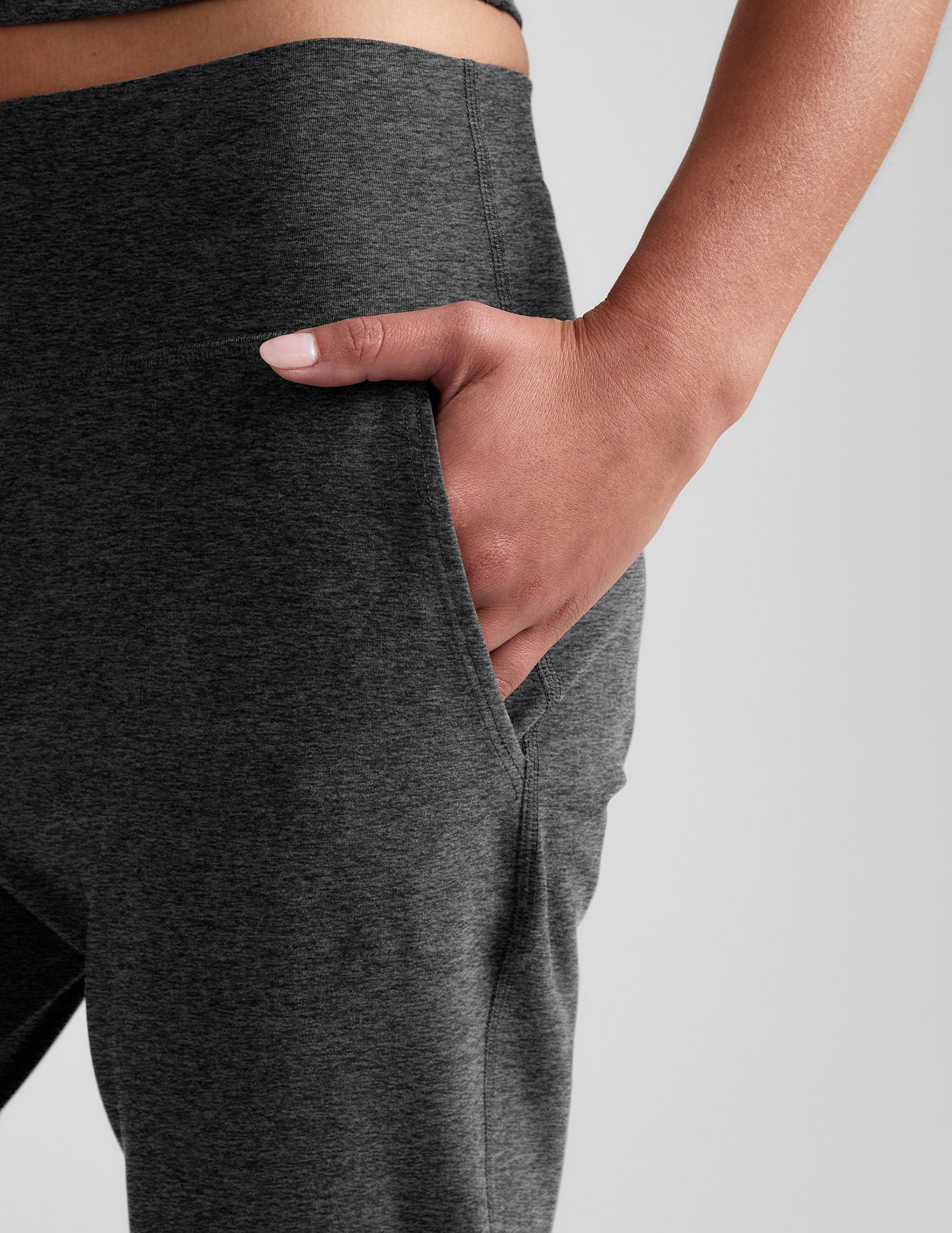 woman wearing a dark gray joggers on a plain background.