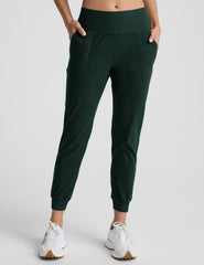 person wearing dark green jogger pants and white sneakers on a plain background.