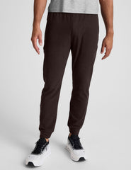 man wearing brown joggers on a plain background.