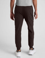 man wearing brown joggers on a plain background.
