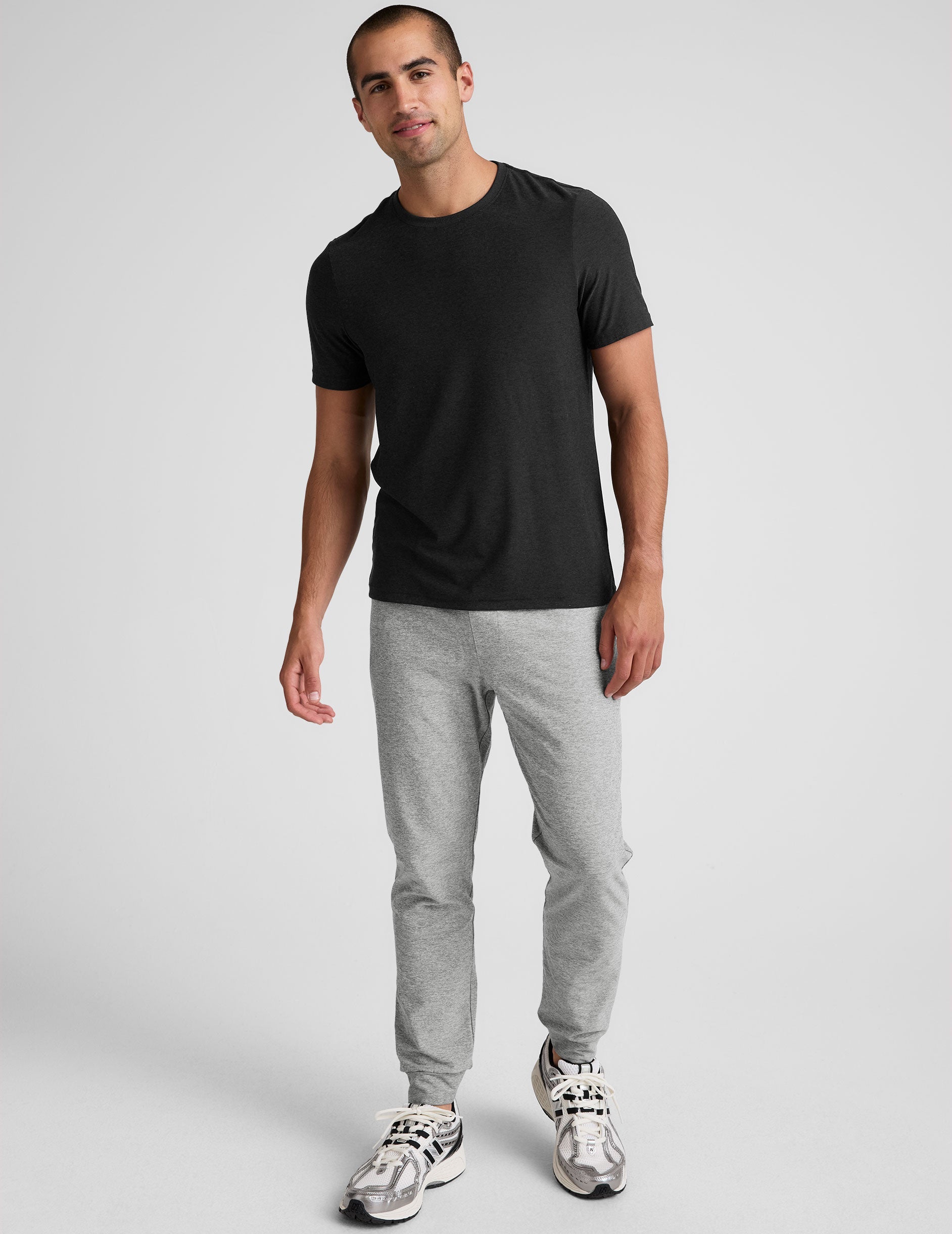 man wearing a black t-shirt and gray sweatpants on a plain background.