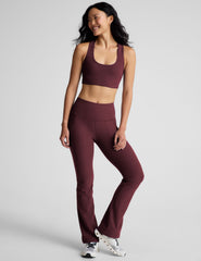 model wearing a maroon sports bra and bootcut pants with pockets on a light gray background.