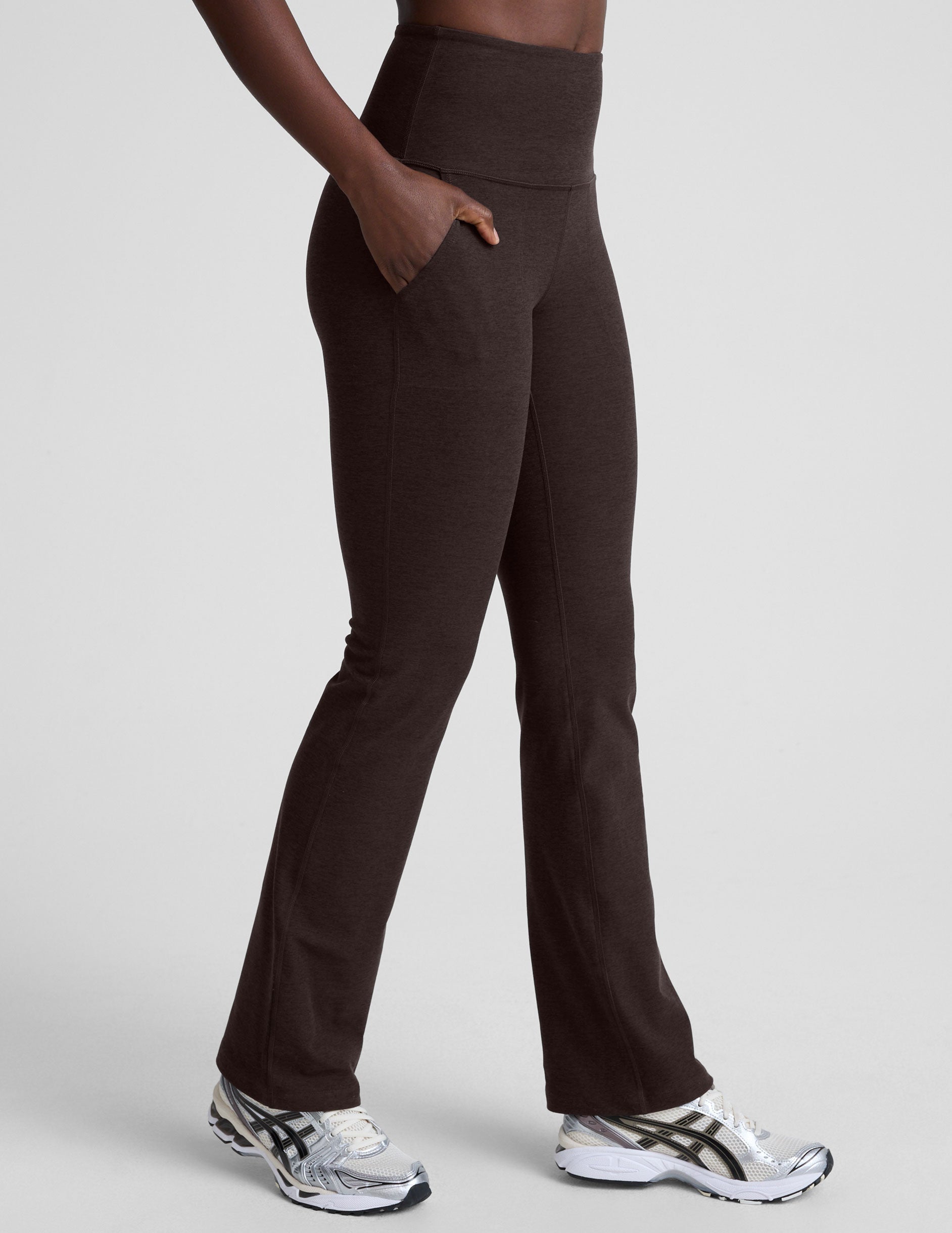 woman wearing a brown sports bra and mid-rise pants on a white background.