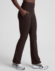 woman wearing a brown sports bra and mid-rise pants on a white background.