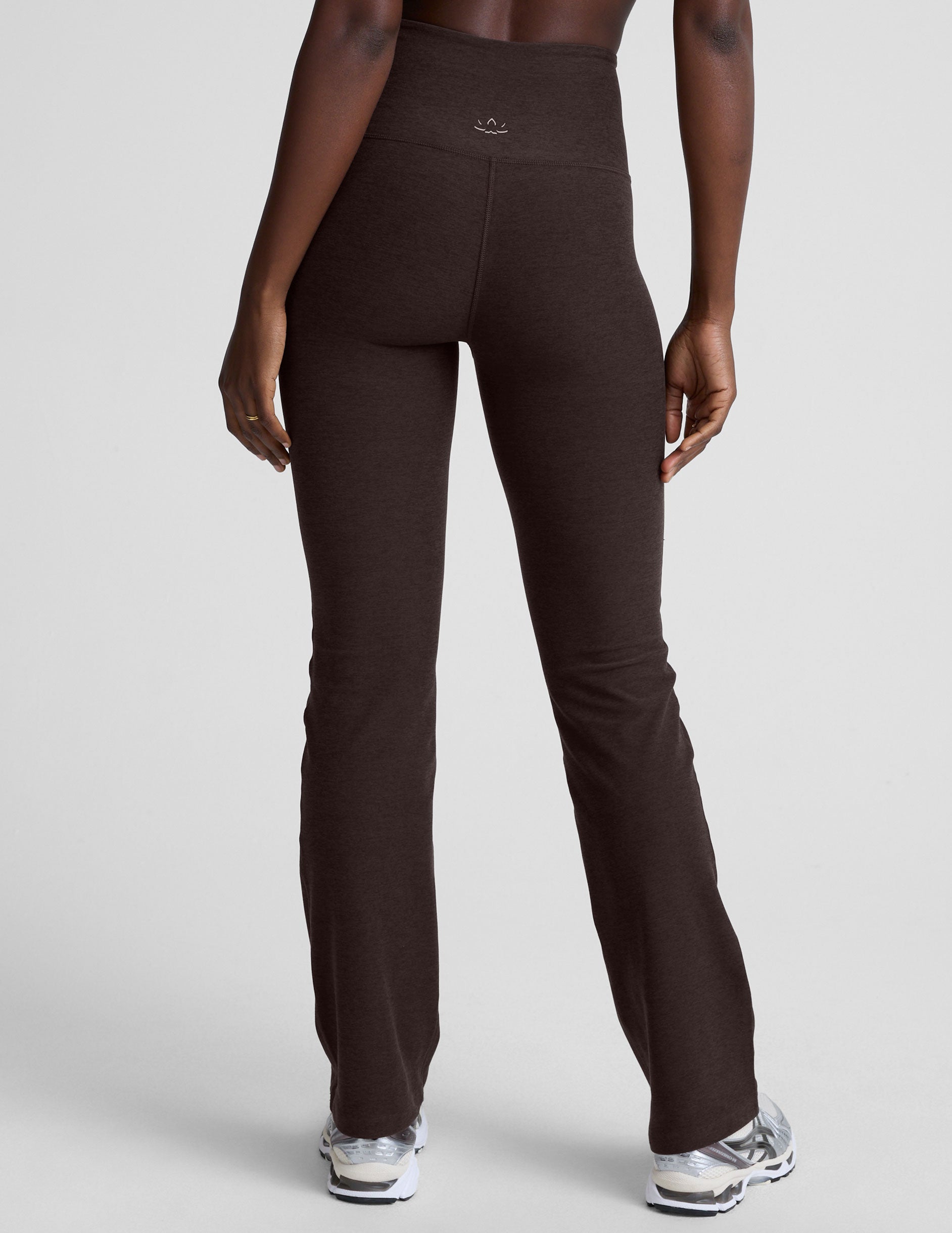 woman wearing a brown sports bra and mid-rise pants on a white background.