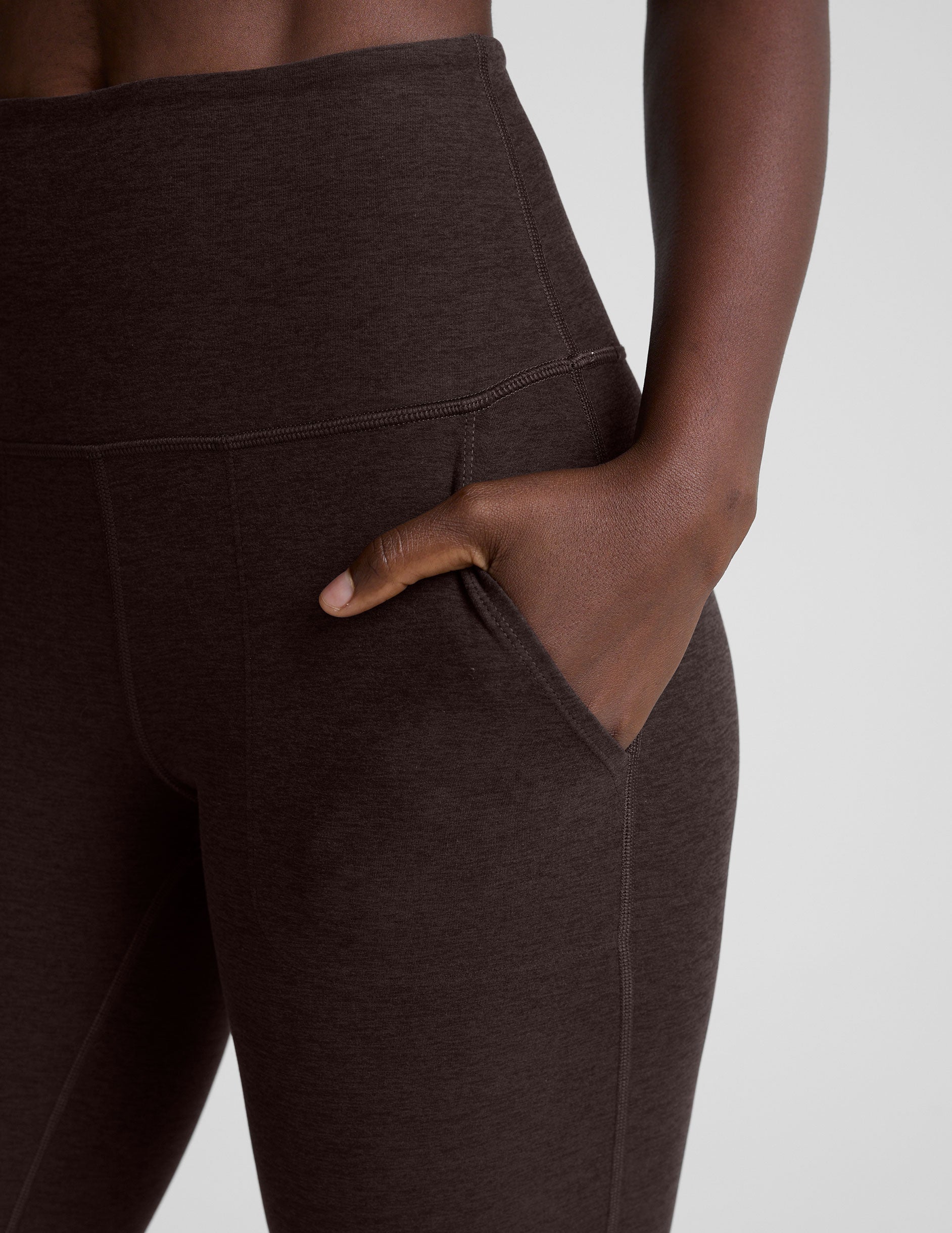 woman wearing a brown sports bra and mid-rise pants on a white background.