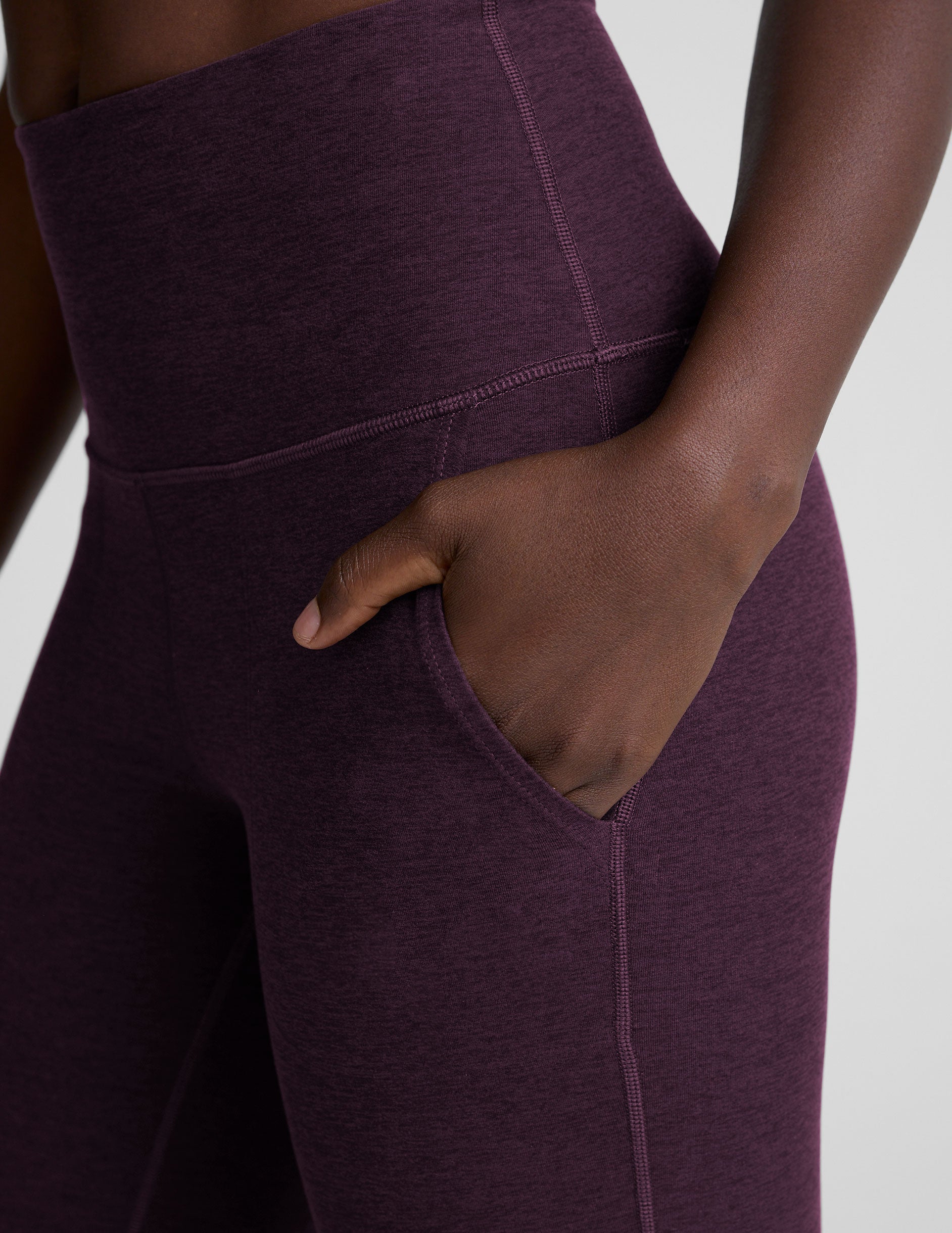 model wearing purple high-waisted bootcut pants with pockets on a plain background.