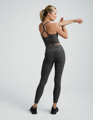 woman wearing a gray cropped tank and long length leggings on a plain background.