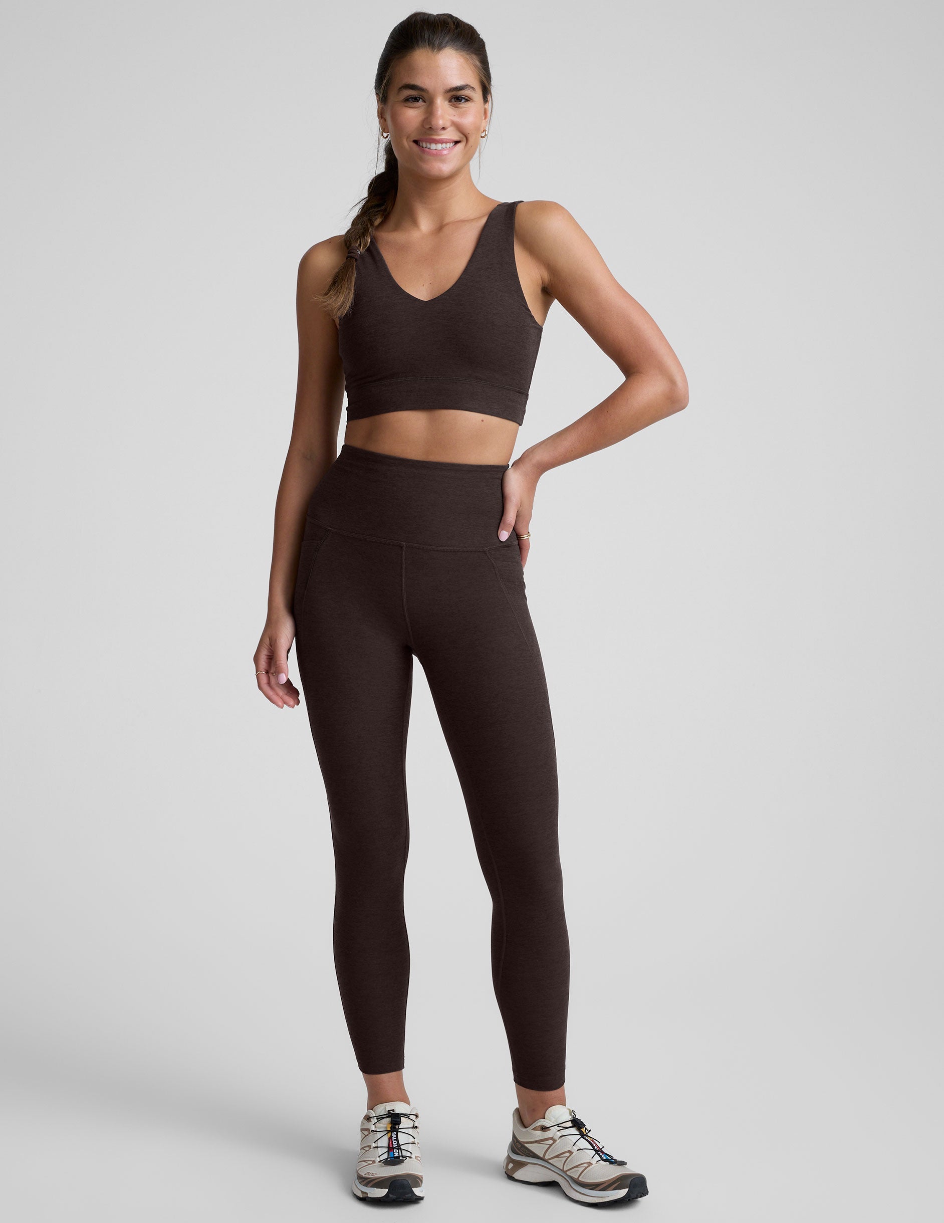 woman wearing a brown high-waisted midi length pocket leggings  with a plain background.