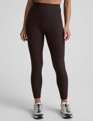 woman wearing a brown high-waisted midi length pocket leggings  with a plain background.
