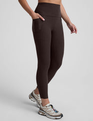 woman wearing a brown high-waisted midi length pocket leggings  with a plain background.