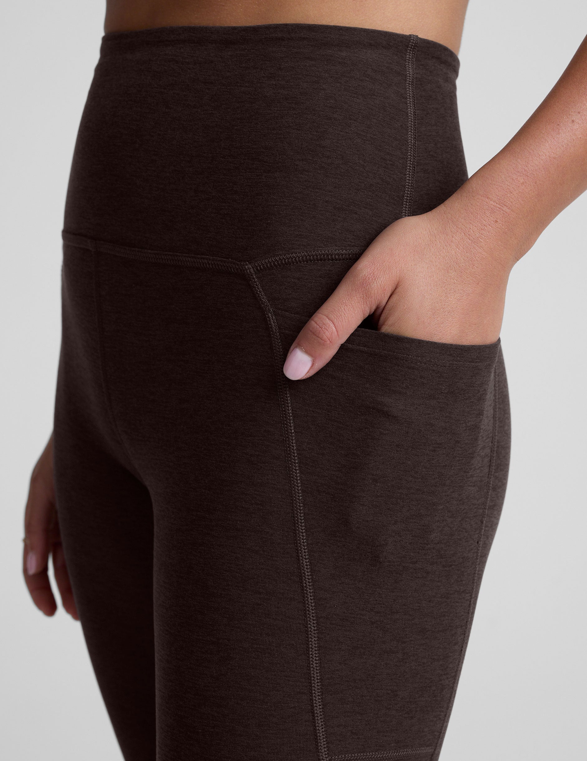 woman wearing a brown high-waisted midi length pocket leggings  with a plain background.