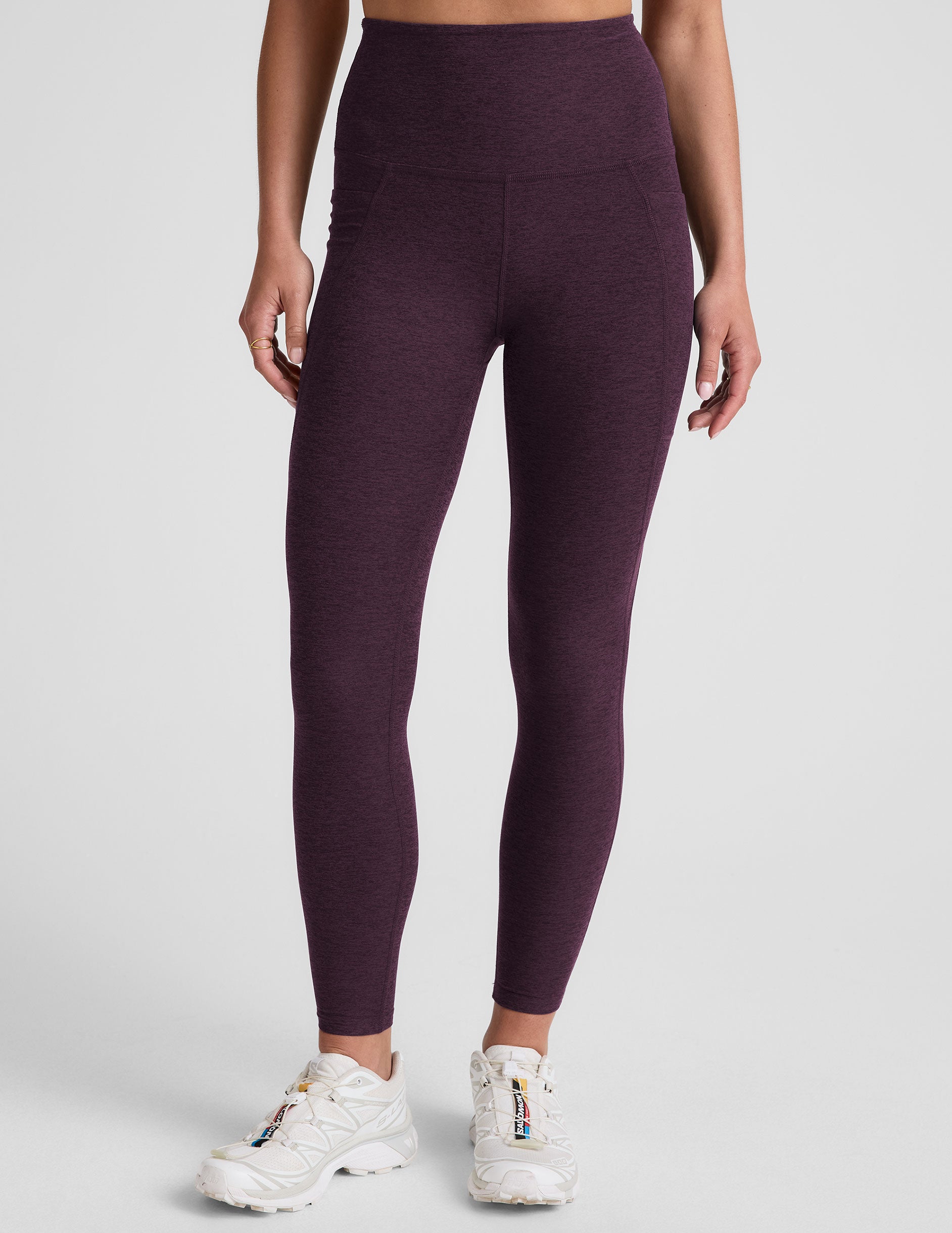 model wearing a purple t-shirt and purple high-waisted midi length leggings with pockets on a light gray background.