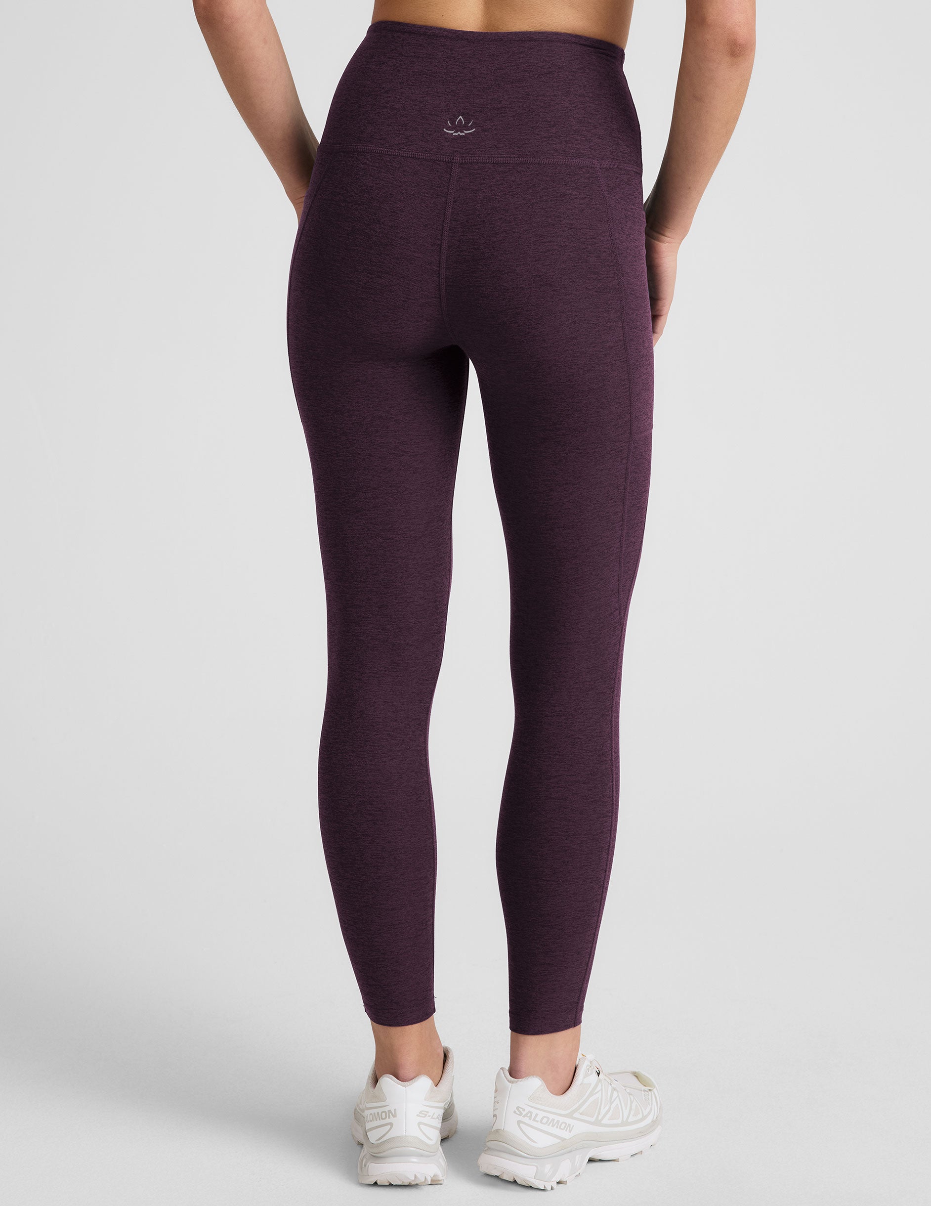 model wearing a purple t-shirt and purple high-waisted midi length leggings with pockets on a light gray background.