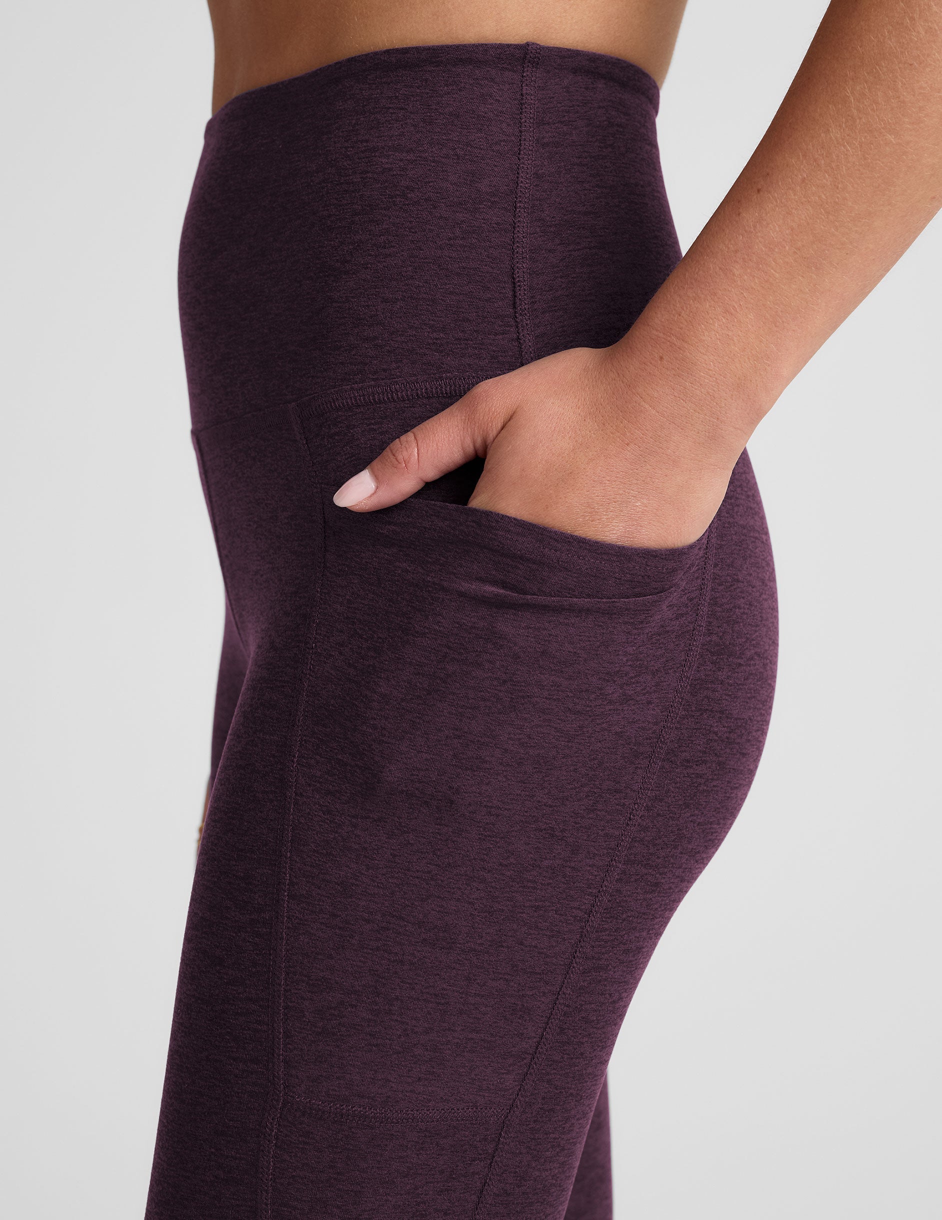 model wearing a purple t-shirt and purple high-waisted midi length leggings with pockets on a light gray background.