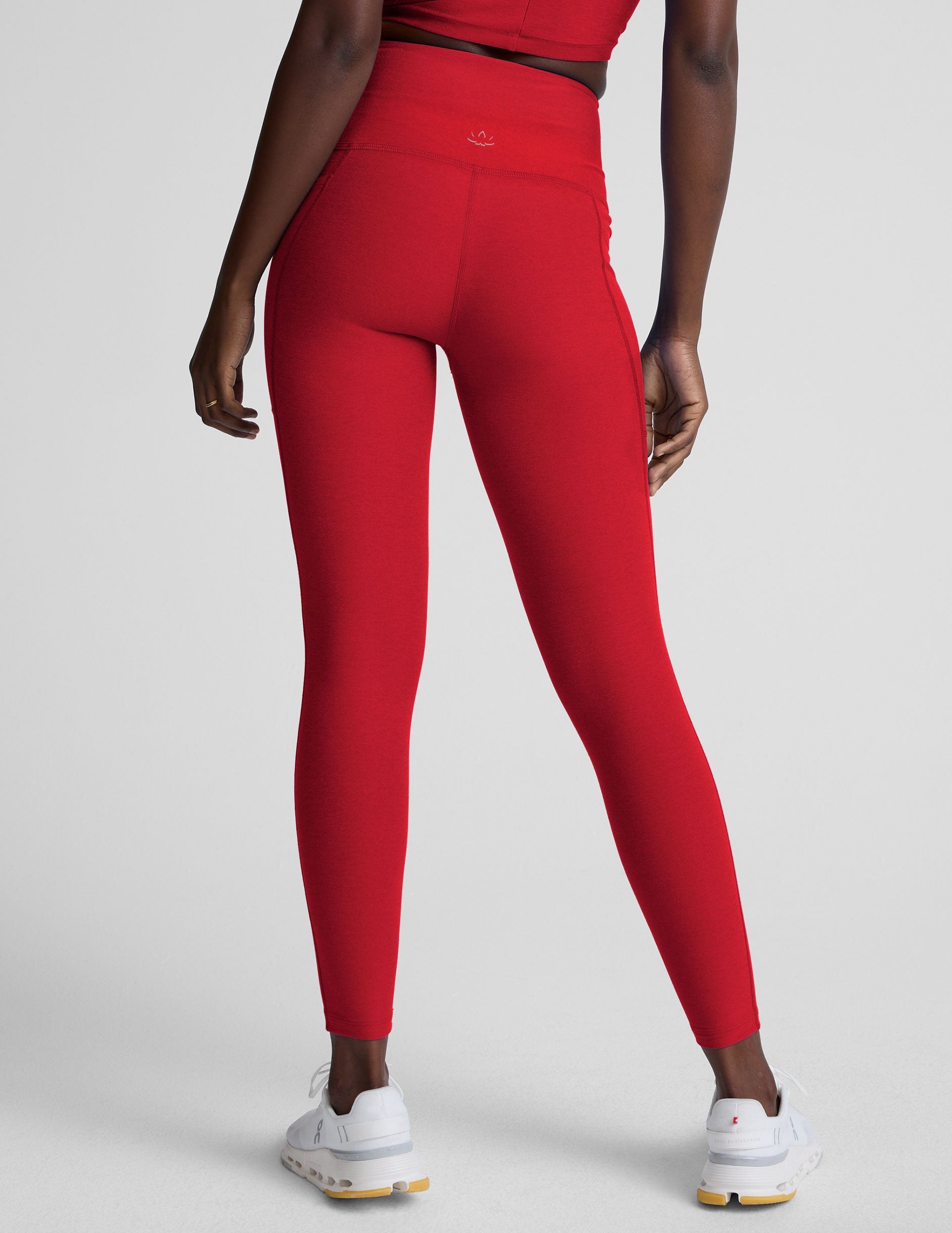 woman wearing a red high-waisted midi length pocket leggings on a plain background.