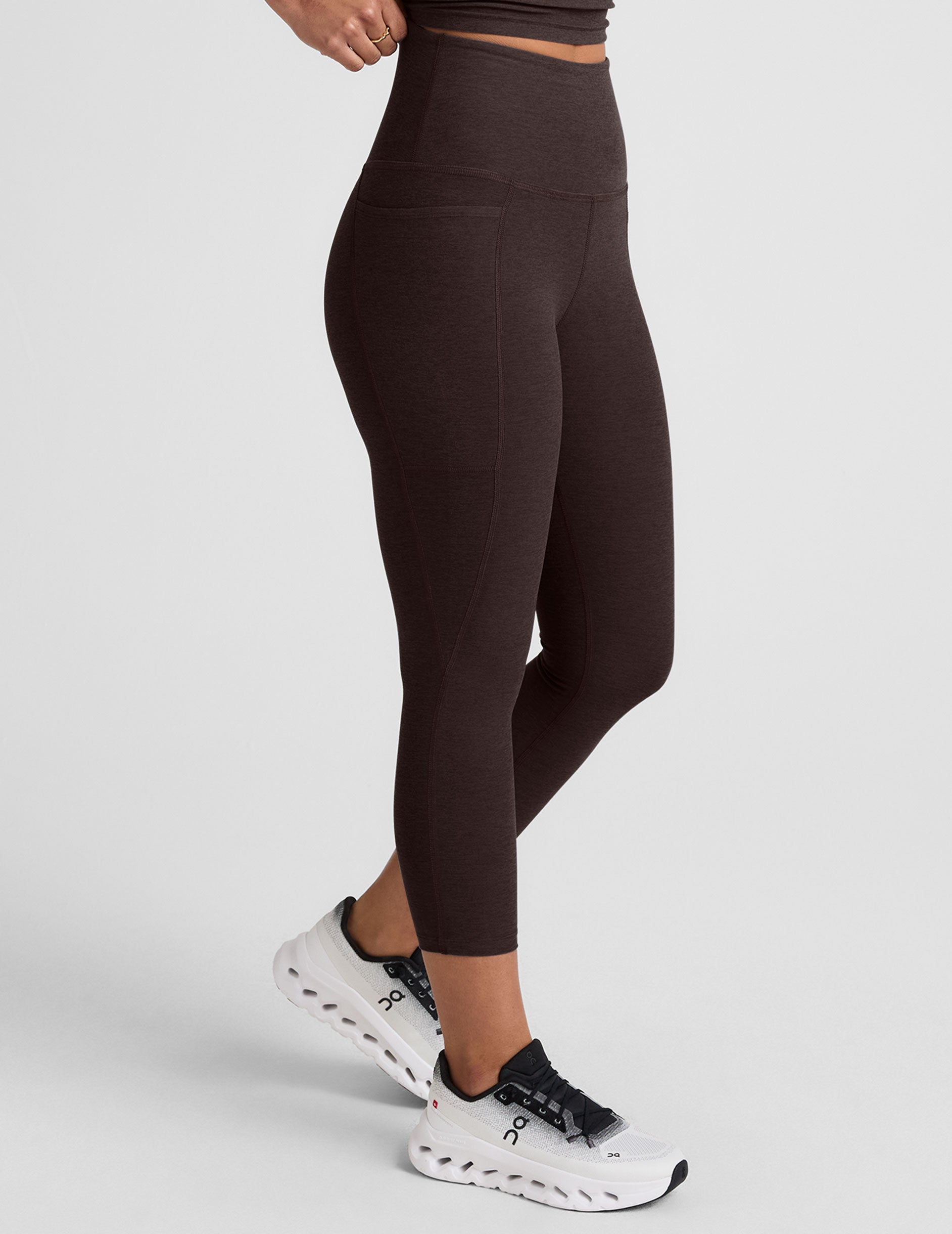 woman wearing a brown capri length leggings with pockets on a plain background.
