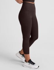woman wearing a brown capri length leggings with pockets on a plain background.