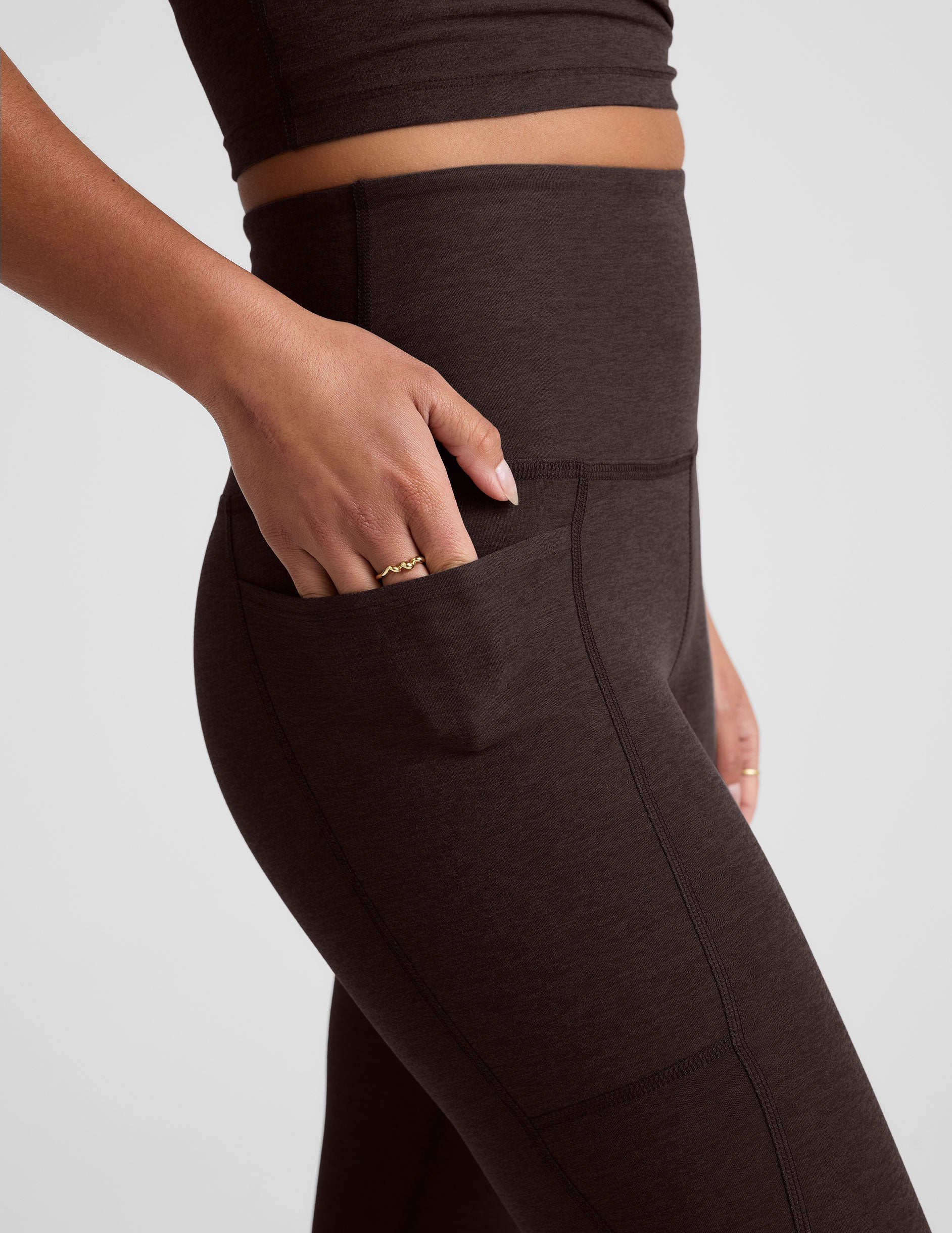 woman wearing a brown capri length leggings with pockets on a plain background.