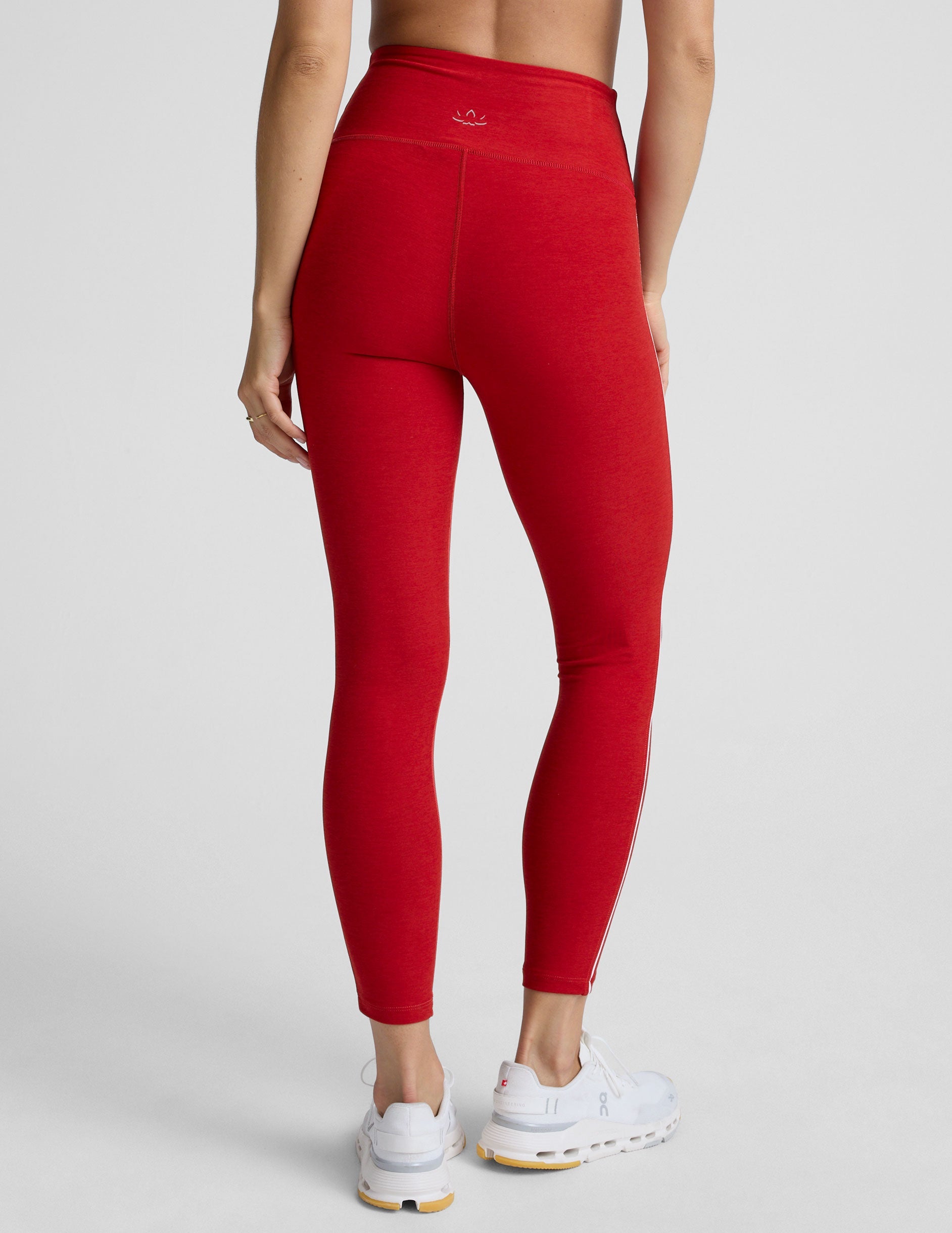 woman in red bra with white piping and red high-waisted midi length leggings with white piping against a plain background.