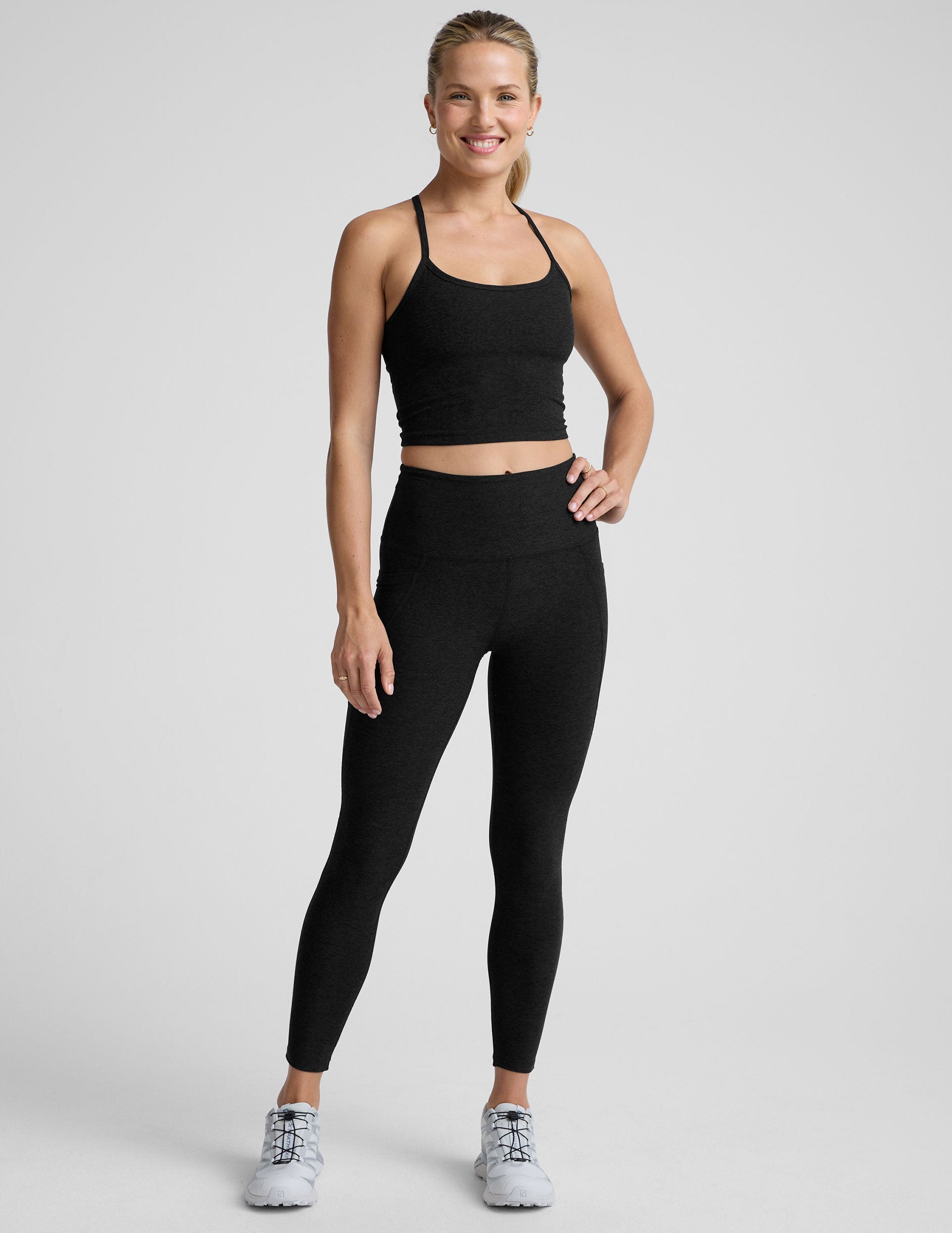 woman wearing a black racerback cropped tank and leggings on a plain background.