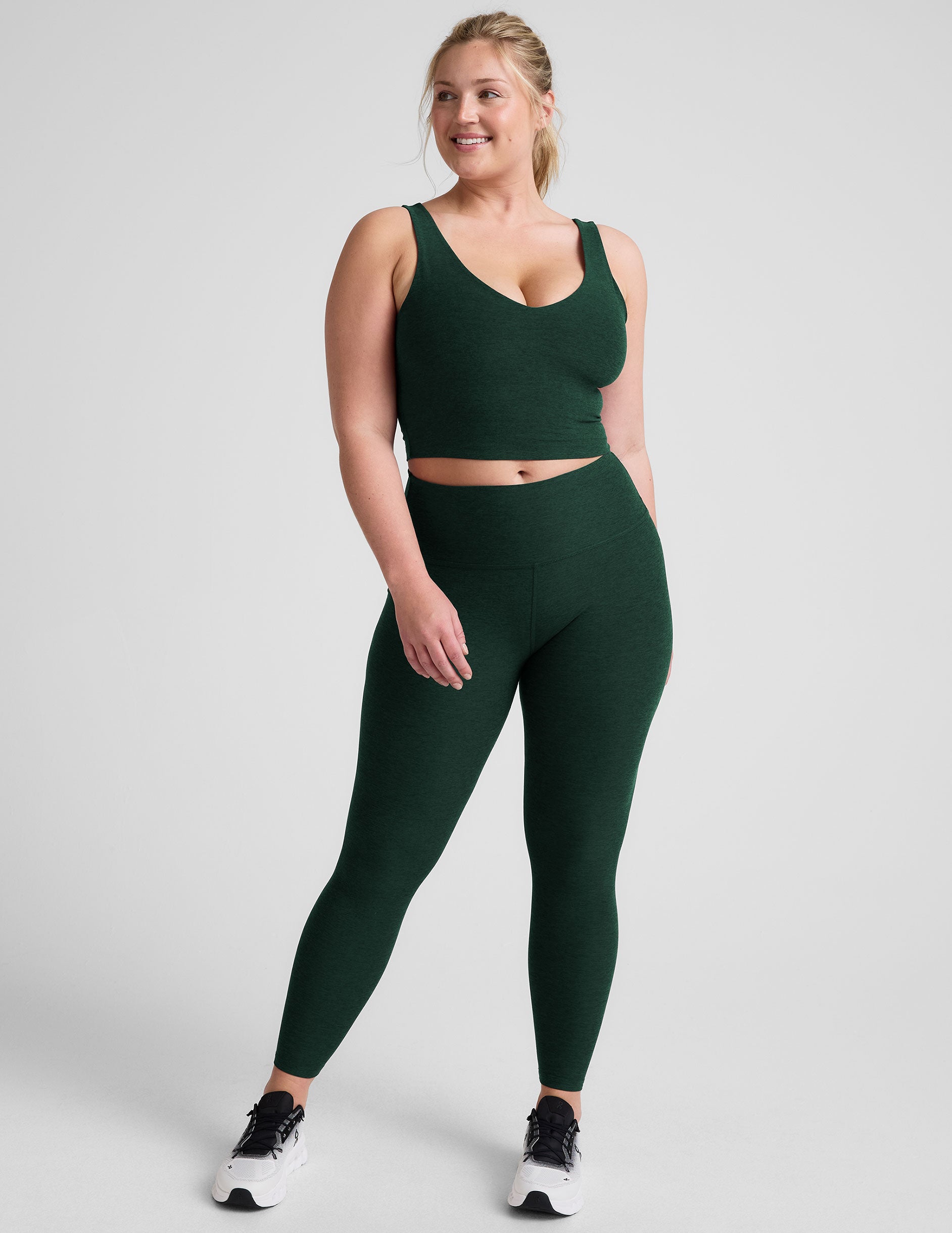 woman wearing a green soft v-neck cropped tank and joggers against a plaind background.