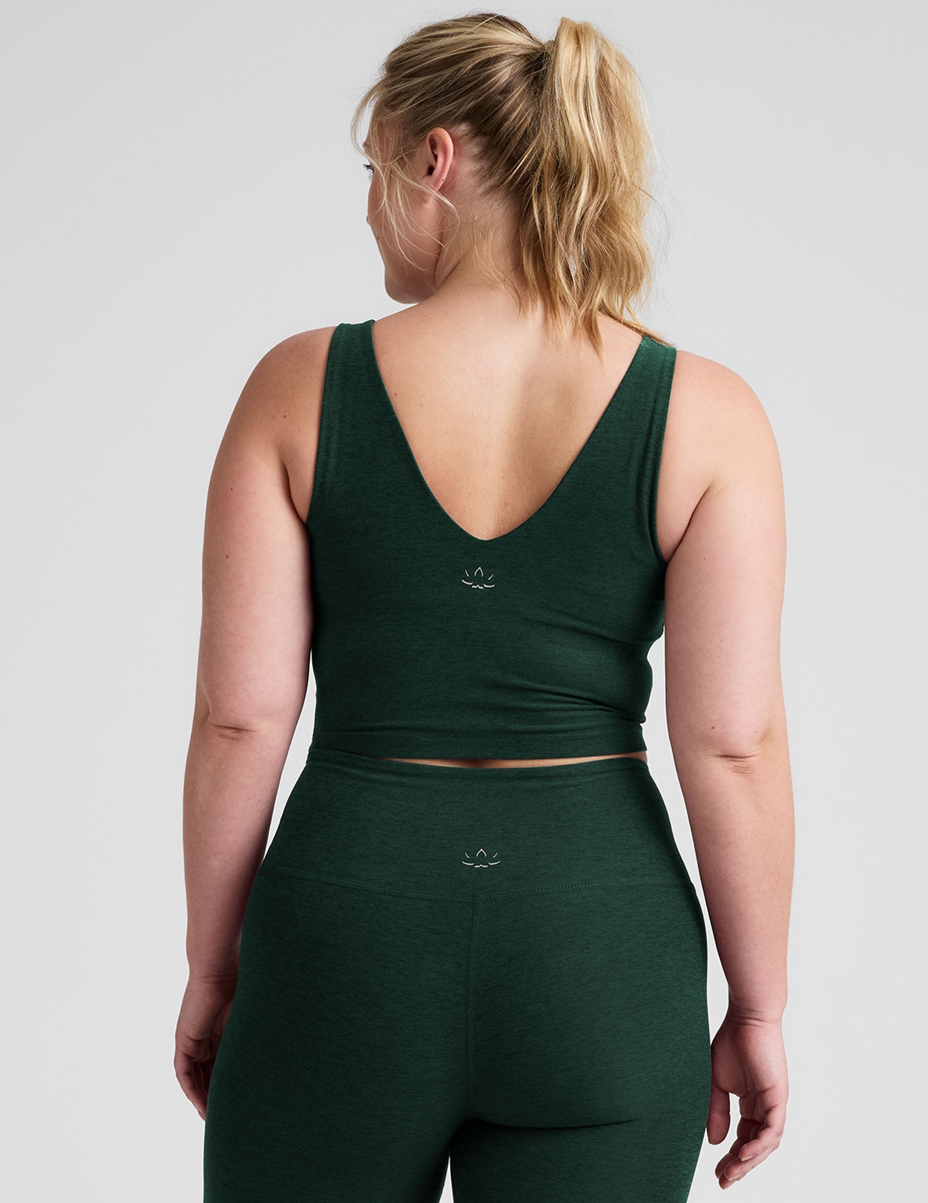 woman wearing a green soft v-neck cropped tank and joggers against a plaind background.