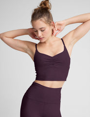 model wearing a purple cropped tank top with shirring at center front and purple high-waisted midi length leggings against a plain background.