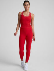 woman wearing a red waist length racerback tank top with white piping on a plain background.