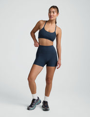 woman wearing a blue slim racerback bra and blue 3" biker shorts against a plain background. 